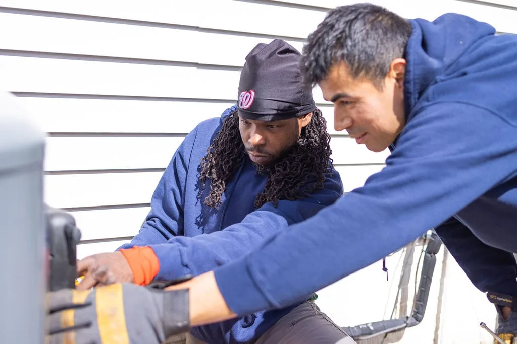 Two HVAC technicians working together on outdoor air-conditioning equipment